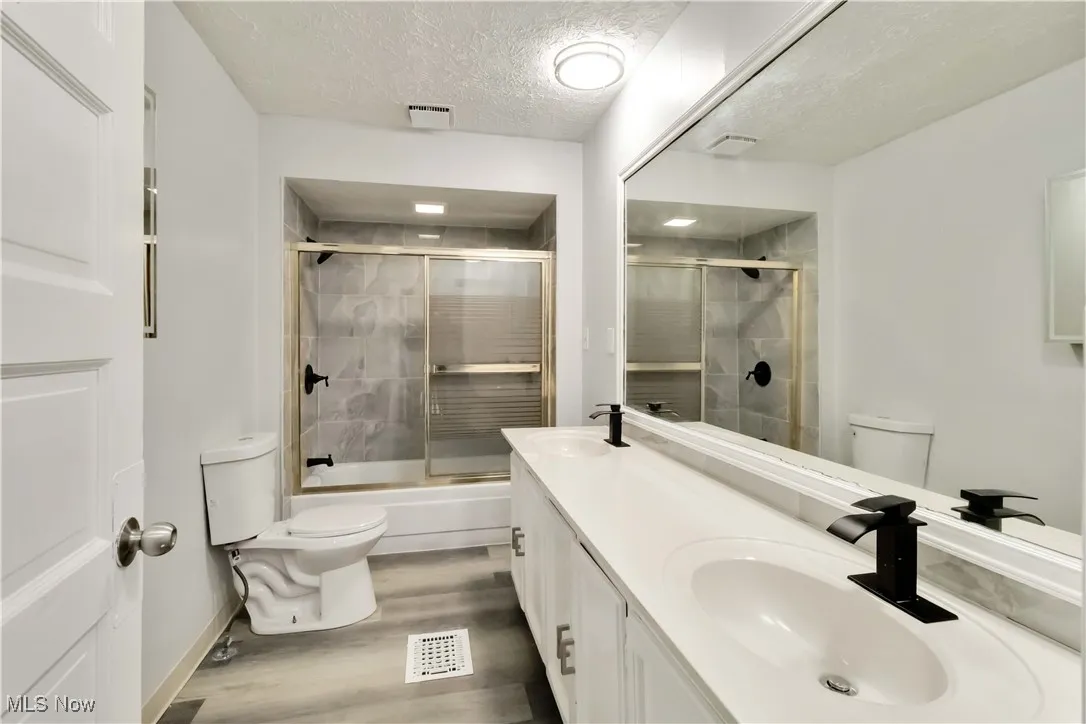 Full bathroom with a textured ceiling, shower / bath combination with glass door, double vanity, and light wood-style floors