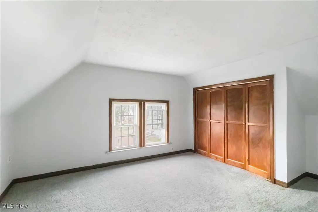 Unfurnished bedroom with vaulted ceiling, a closet, and light carpet