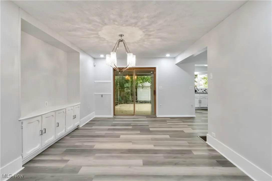 Unfurnished dining area with a chandelier, light wood finished floors, a textured ceiling, and recessed lighting