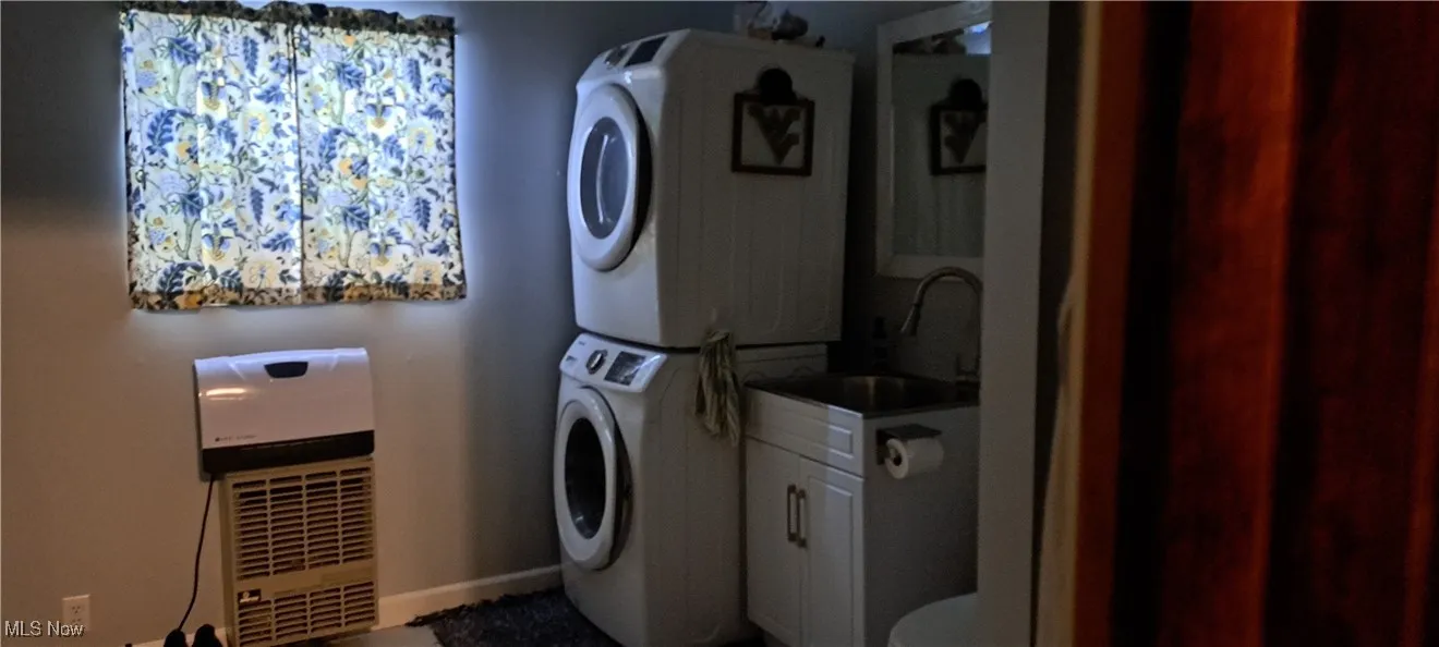 Laundry area with stacked washing machine and dryer, cabinet space, and heating unit
