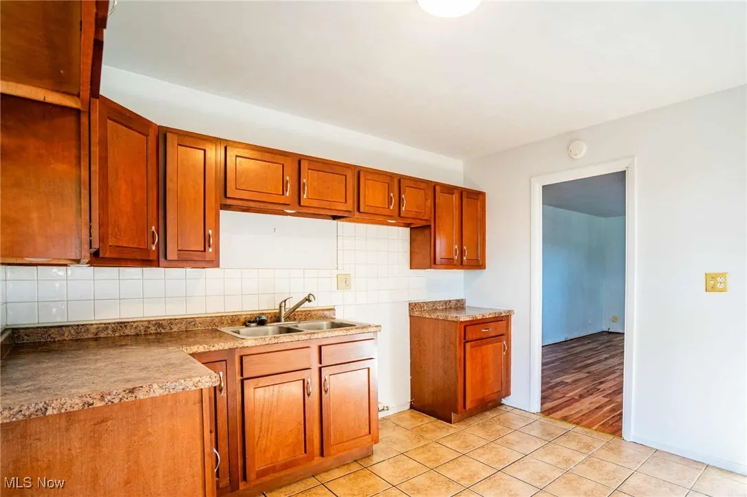 Kitchen with backsplash, brown cabinetry, light tile patterned floors, and light countertops