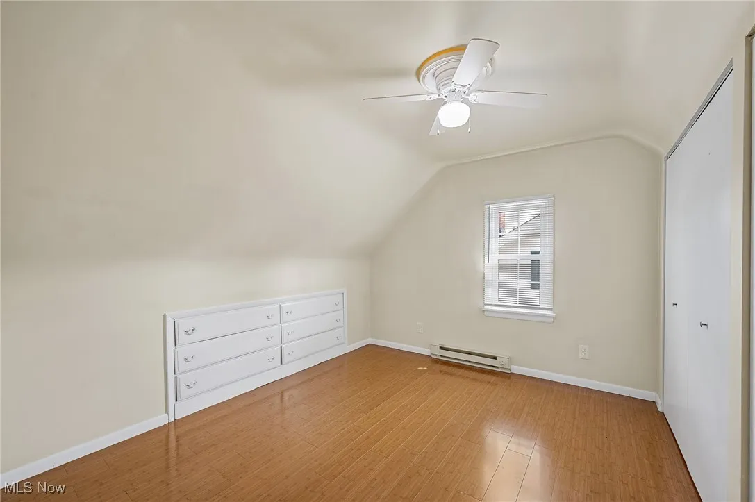 Additional third floor bedroom space featuring lofted ceiling, a baseboard radiator, and wood finished floors