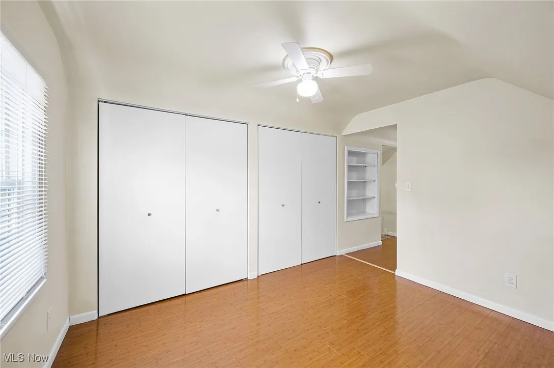 Unfurnished bedroom featuring multiple closets, wood finished floors, ceiling fan, and lofted ceiling