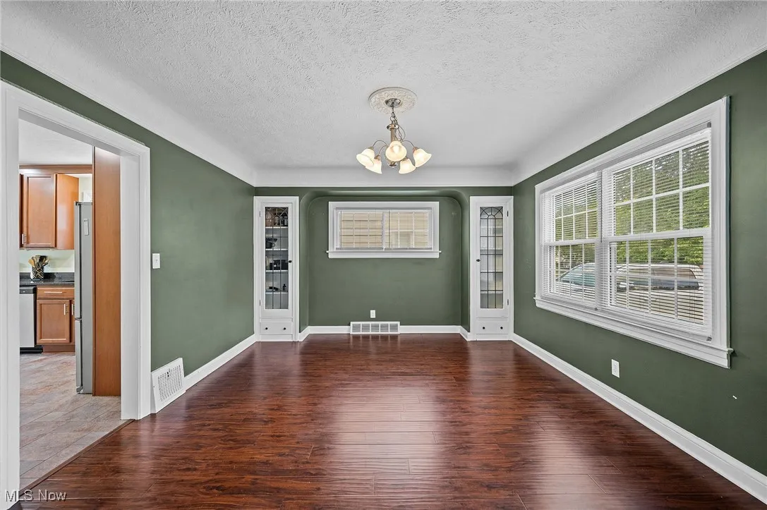 Unfurnished dining area featuring a chandelier, a textured ceiling, and dark wood-style floors