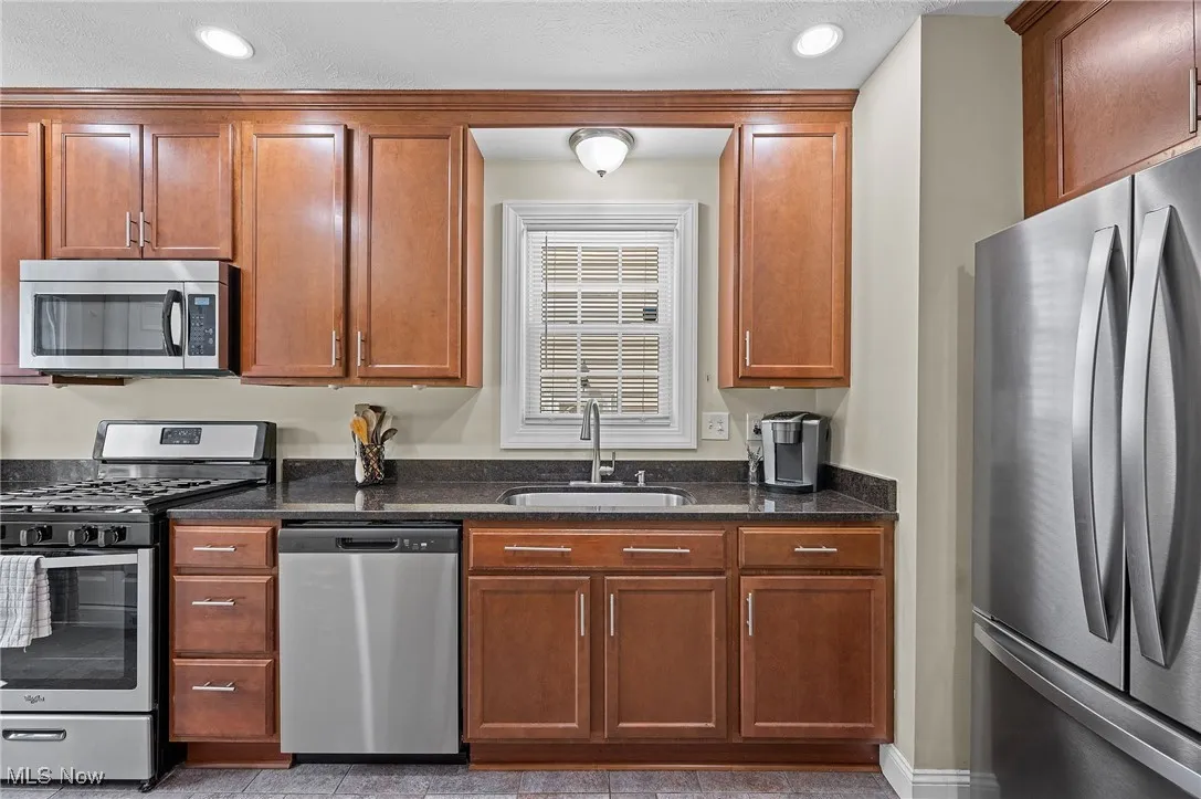 Kitchen with stainless steel appliances, dark stone countertops, recessed lighting, and brown cabinetry