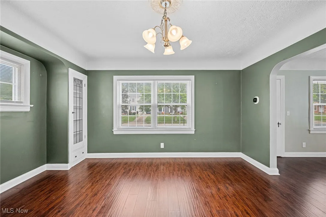 Empty room featuring arched walkways, dark wood-type flooring, a textured ceiling, and a chandelier