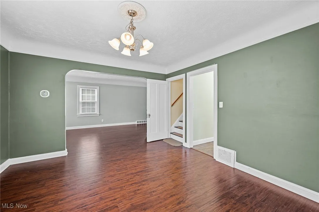 Empty room featuring dark wood-style floors, stairway, a textured ceiling, arched walkways, and a chandelier