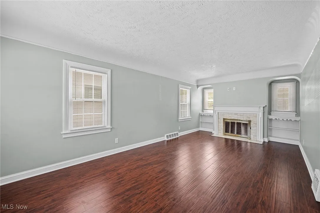 Unfurnished living room with a textured ceiling, a fireplace with flush hearth, and dark wood finished floors
