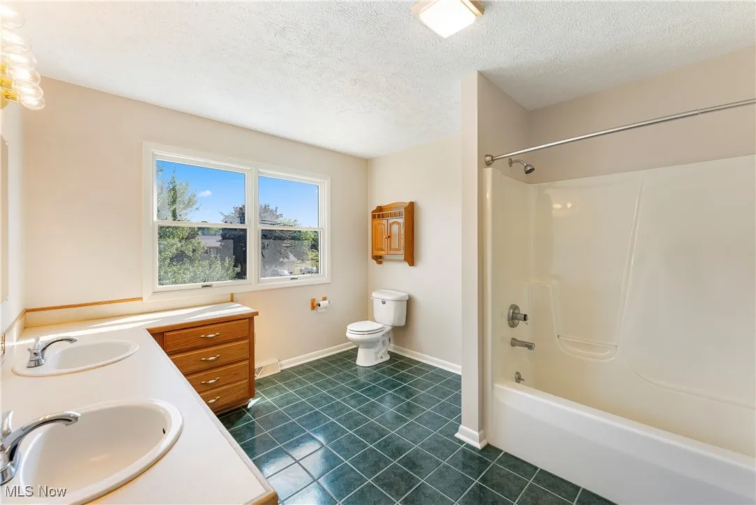 Bathroom featuring shower / bath combination, a textured ceiling, dark tile patterned flooring, and double vanity