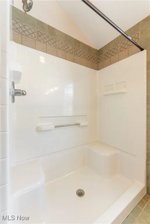 Full bath with a stall shower, a textured ceiling, tile patterned flooring, and vaulted ceiling