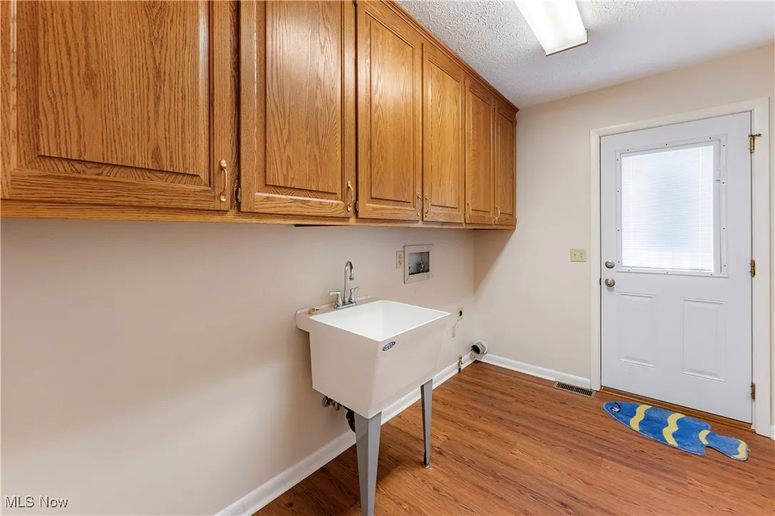 Washroom with light wood-style flooring, a textured ceiling, hookup for a washing machine, and cabinet space
