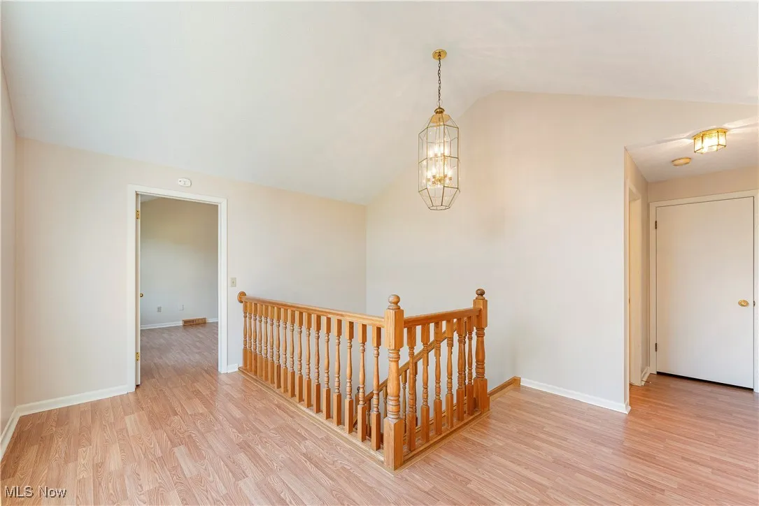 Corridor featuring an upstairs landing, light wood-style floors, lofted ceiling, and a chandelier