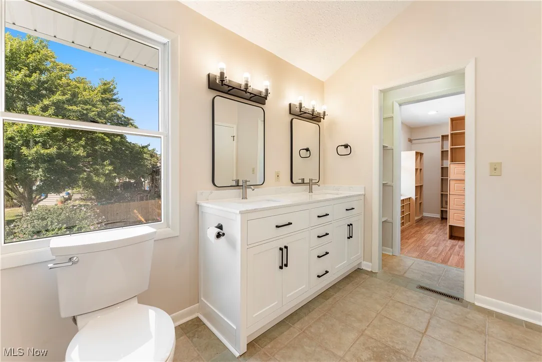 Bathroom featuring a double vanity, light tile patterned floors white cabinetry and quartz countertops