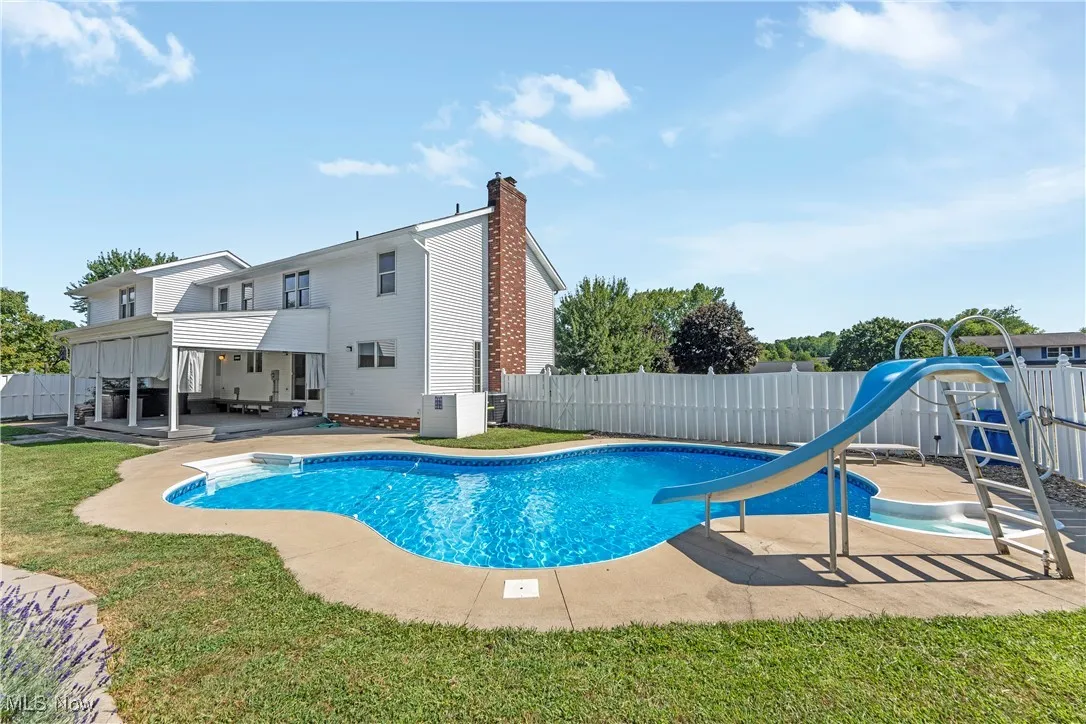 View of swimming pool with a water slide, a fenced backyard, and a patio area