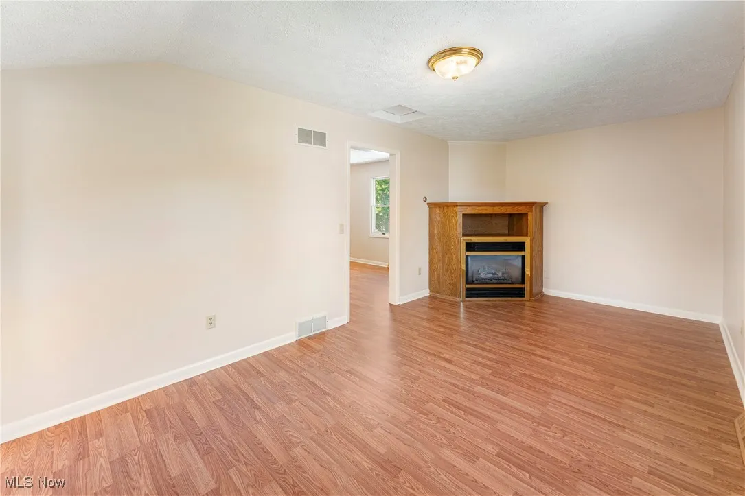 Bedroom featuring light wood look laminate floors, a textured ceiling, and a glass covered decorative fireplace