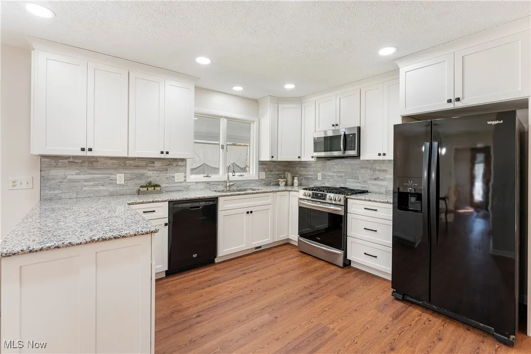 Kitchen featuring black appliances, granite countertops, white cabinetry, a textured ceiling, and LVP floors