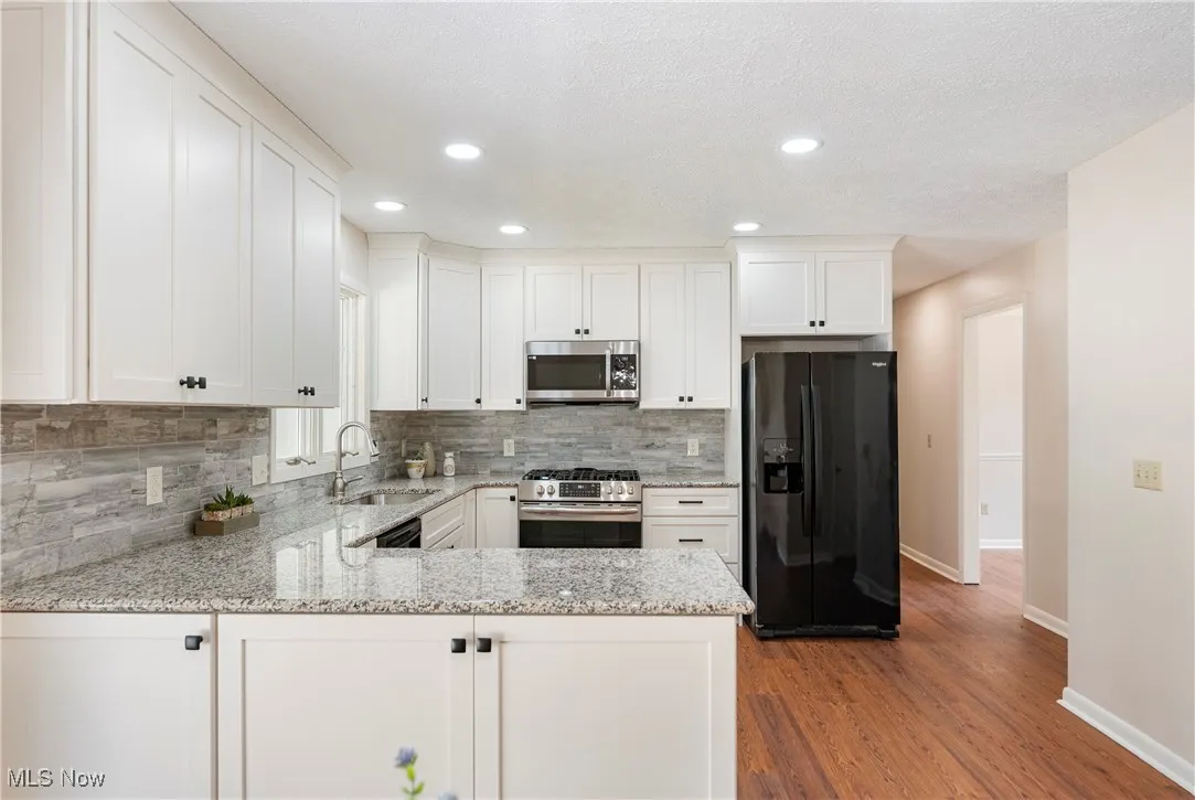 Kitchen featuring appliances, granite countertops, white cabinets, a peninsula, and recessed lighting