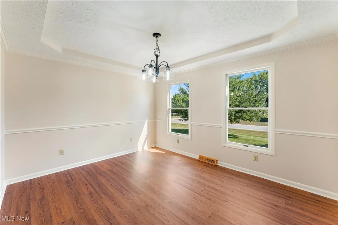 Unfurnished dining area with a tray ceiling, wood finished floors, a chandelier, crown molding, and a textured ceiling