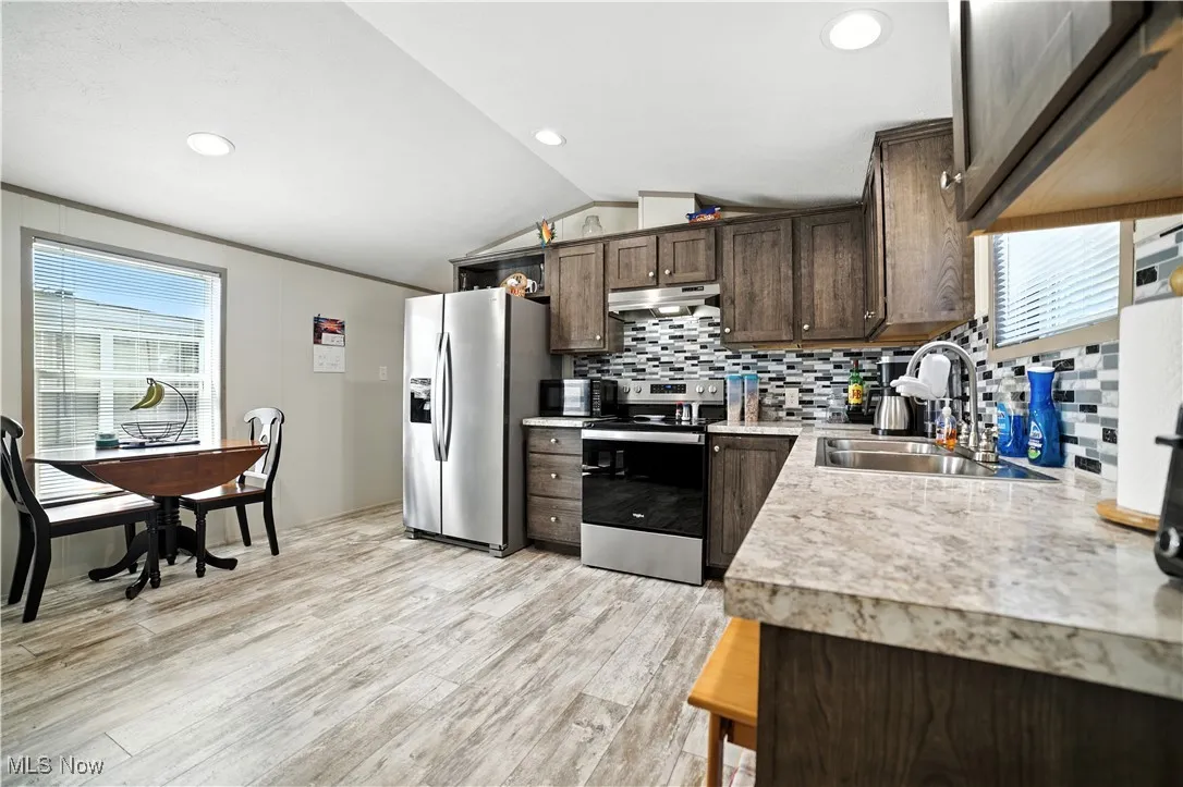 Kitchen with plenty of natural light, dark brown cabinets, light countertops, stainless steel appliances, and lofted ceiling