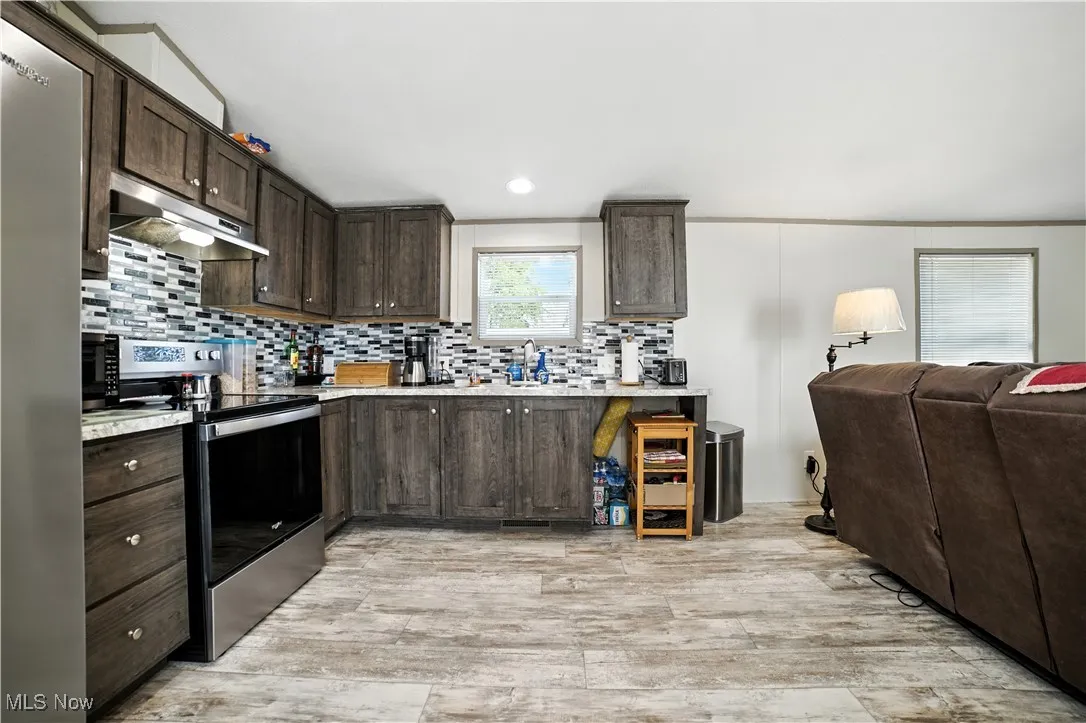 Kitchen with dark brown cabinetry, light countertops, appliances with stainless steel finishes, under cabinet range hood, and tasteful backsplash