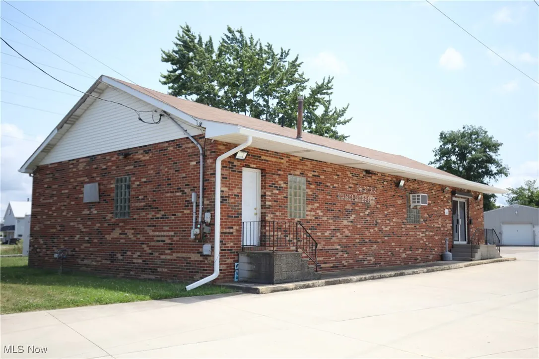 View of side of property with entry steps, a garage, brick siding, and an outbuilding