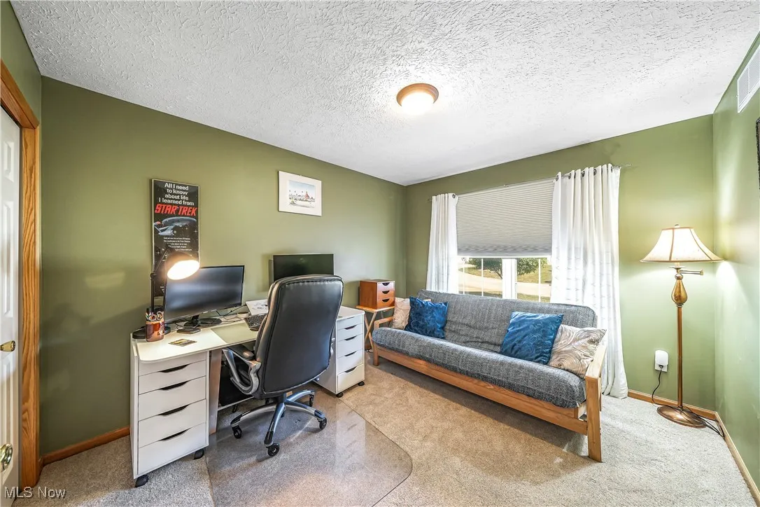 Carpeted office featuring baseboards and a textured ceiling