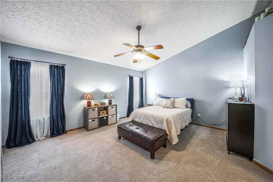 Carpeted bedroom with vaulted ceiling, ceiling fan, and a textured ceiling