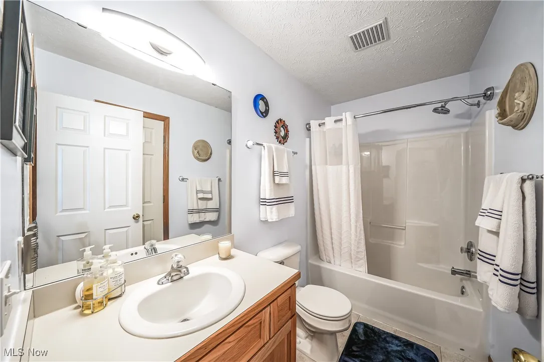 Bathroom featuring shower / tub combo, a textured ceiling, and vanity