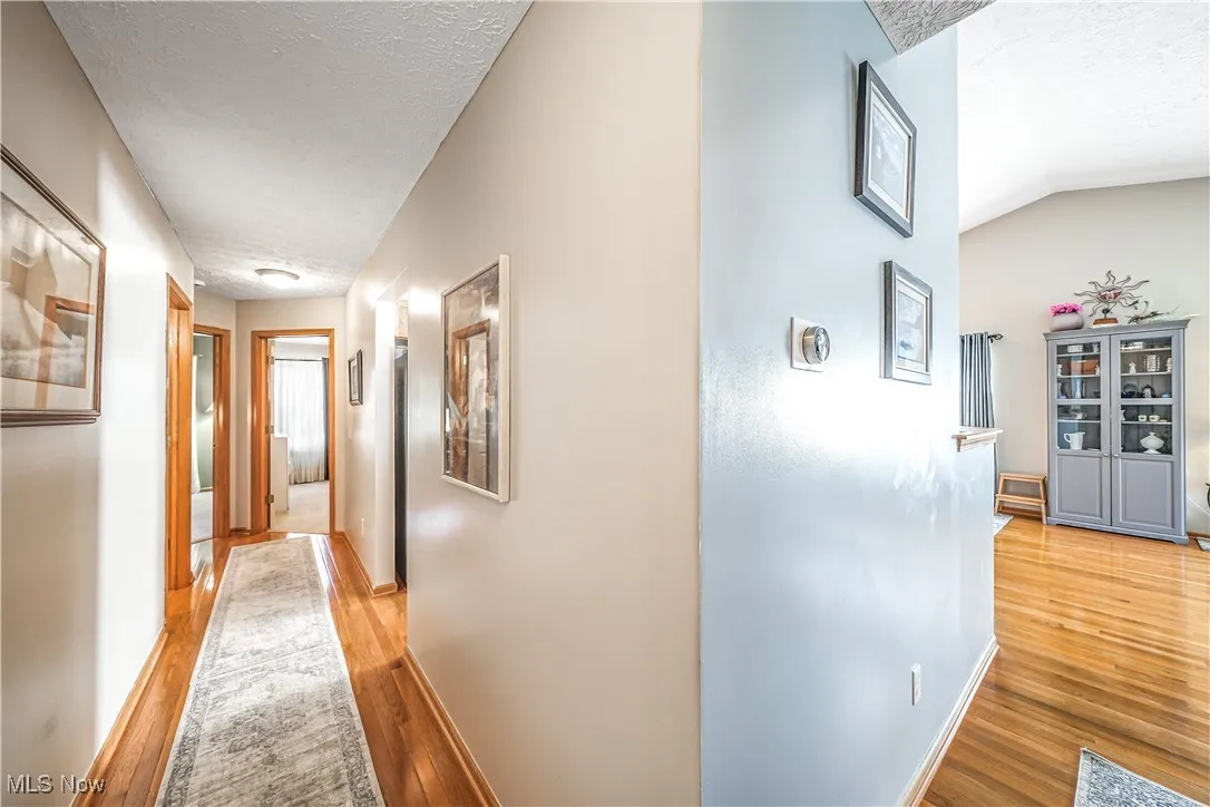 Hall with light wood-style flooring, a textured ceiling, and lofted ceiling
