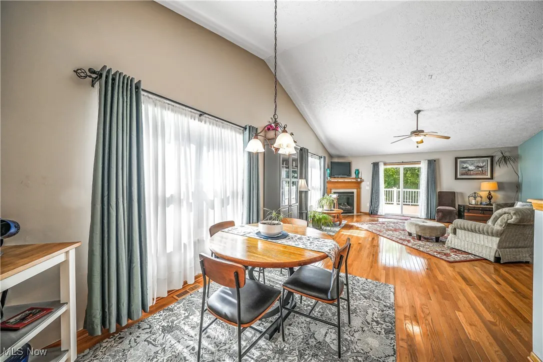 Dining room with a glass covered fireplace, wood-type flooring, lofted ceiling, a textured ceiling, and ceiling fan