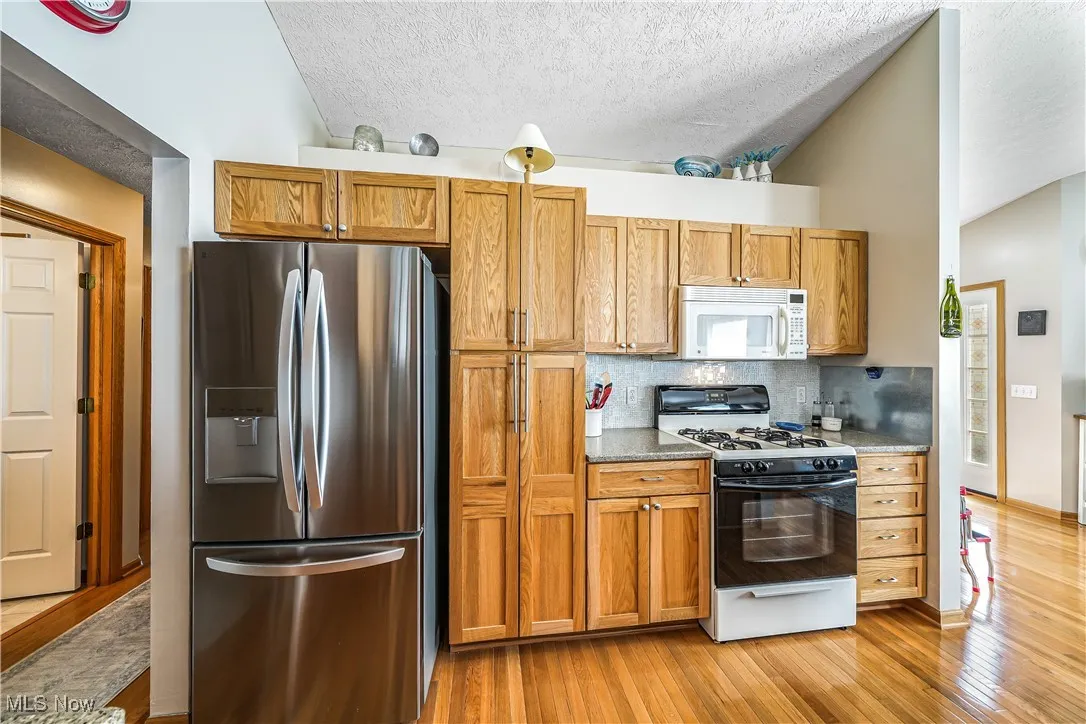 Kitchen featuring white appliances, light wood-type flooring, brown cabinetry, a textured ceiling, and vaulted ceiling