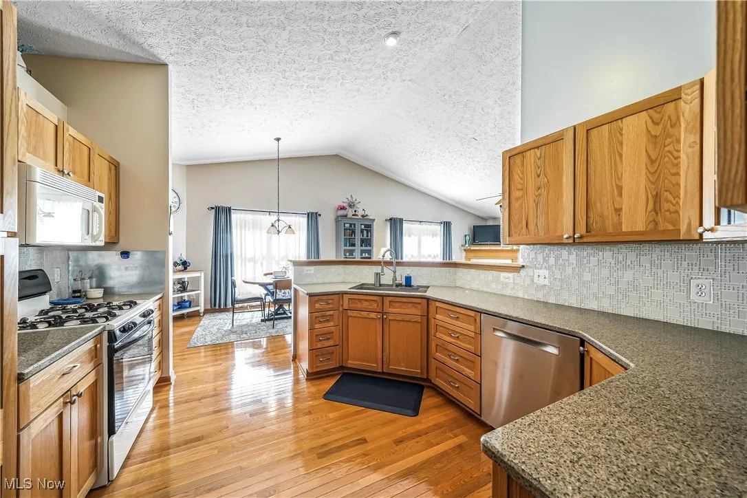 Kitchen featuring backsplash, gas stove, white microwave, hanging light fixtures, and brown cabinets