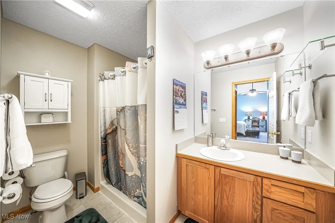 Full bath featuring light tile patterned flooring, a textured ceiling, a shower stall, vanity, and ensuite bathroom
