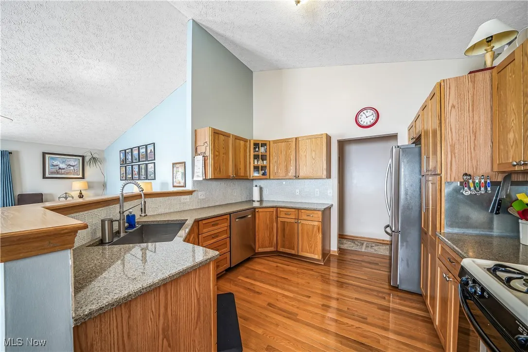 Kitchen featuring brown cabinetry, light stone countertops, a peninsula, stainless steel appliances, and light wood-style floors