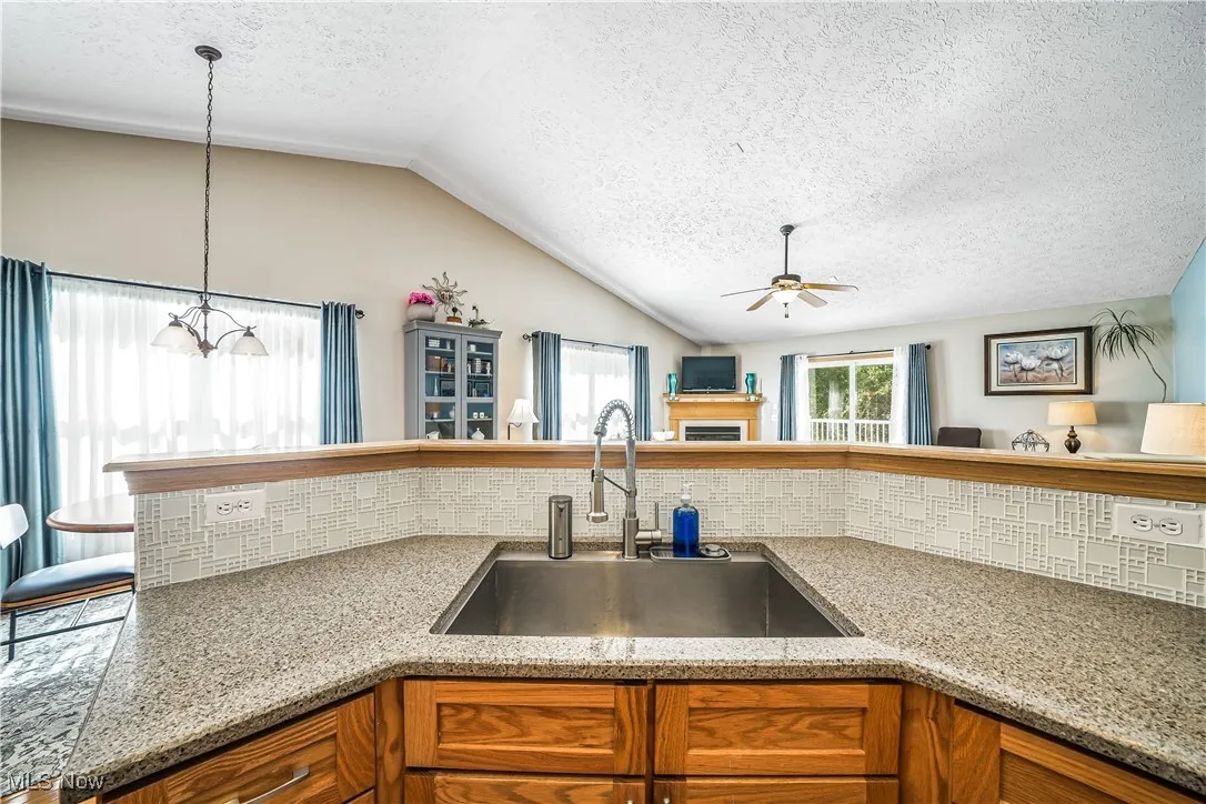 Kitchen with brown cabinets, a textured ceiling, backsplash, vaulted ceiling, and pendant lighting