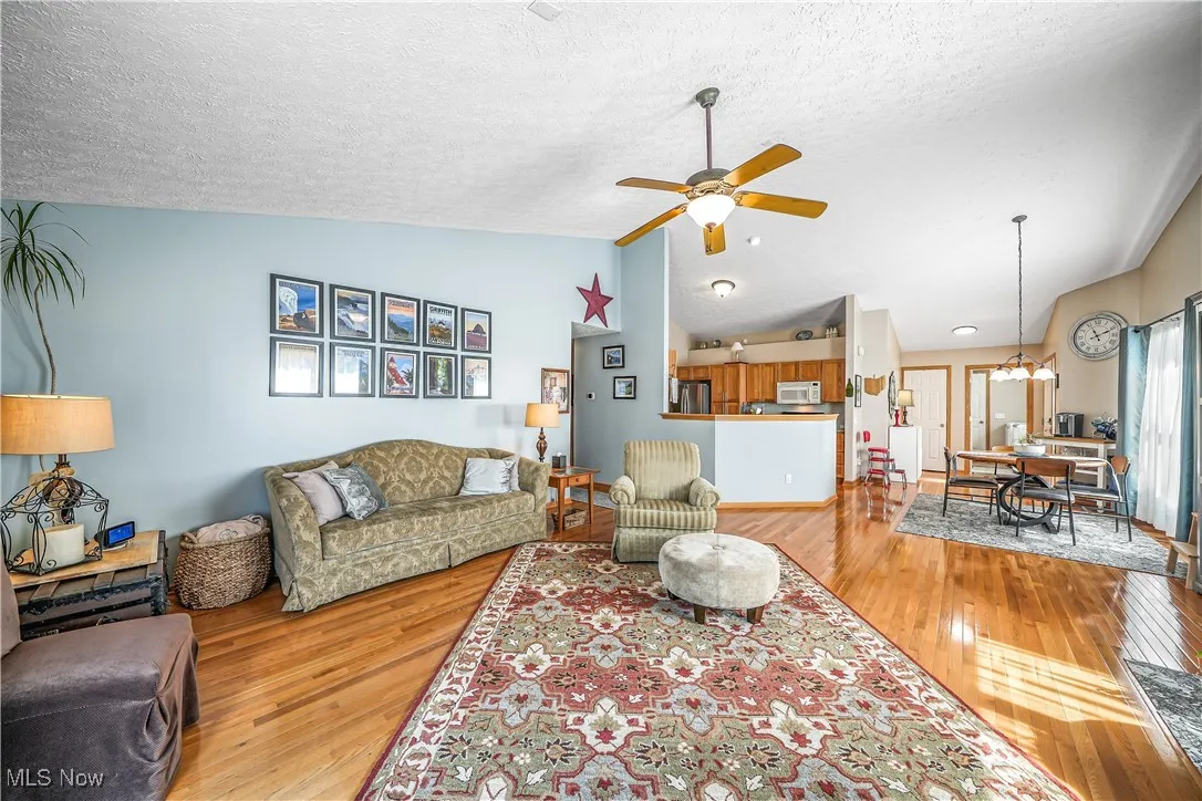 Living room featuring lofted ceiling, light wood finished floors, a ceiling fan, a textured ceiling, and a chandelier