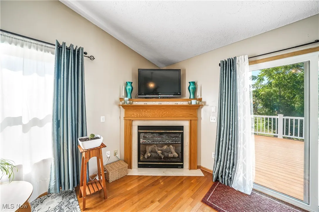 Living room featuring wood finished floors, lofted ceiling, a textured ceiling, and a fireplace with flush hearth