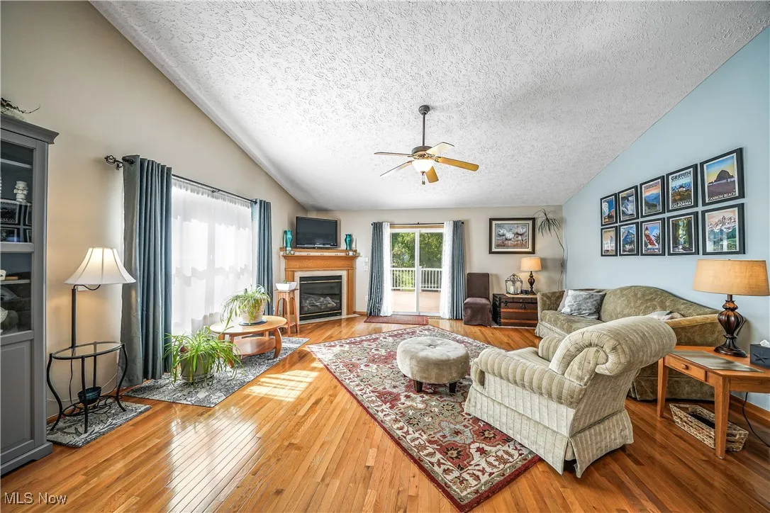 Living area with vaulted ceiling, wood-type flooring, a glass covered fireplace, a textured ceiling, and ceiling fan
