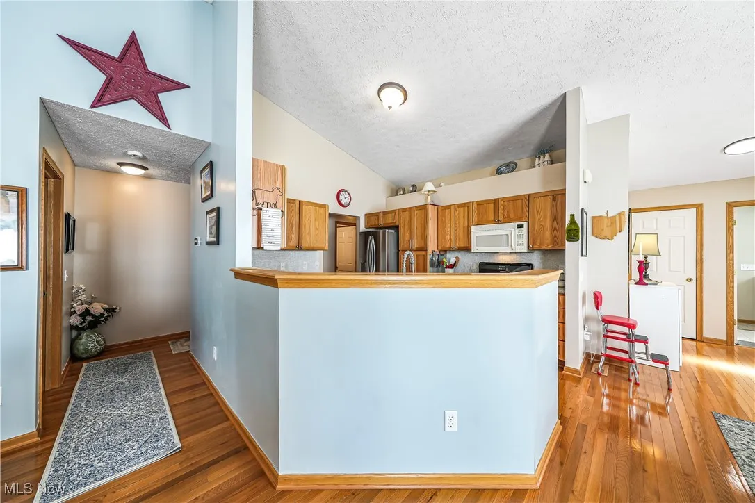 Kitchen featuring a textured ceiling, brown cabinetry, light wood-style floors, vaulted ceiling, and a peninsula