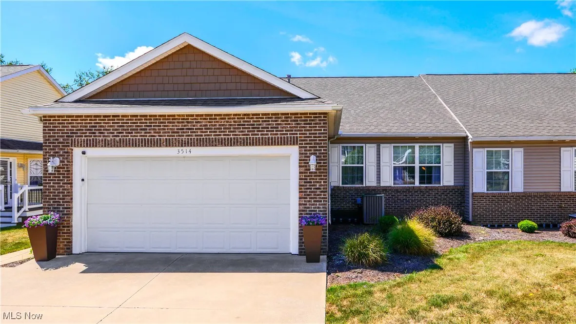 Ranch-style home featuring brick siding, a shingled roof, an attached garage, driveway, and a front lawn