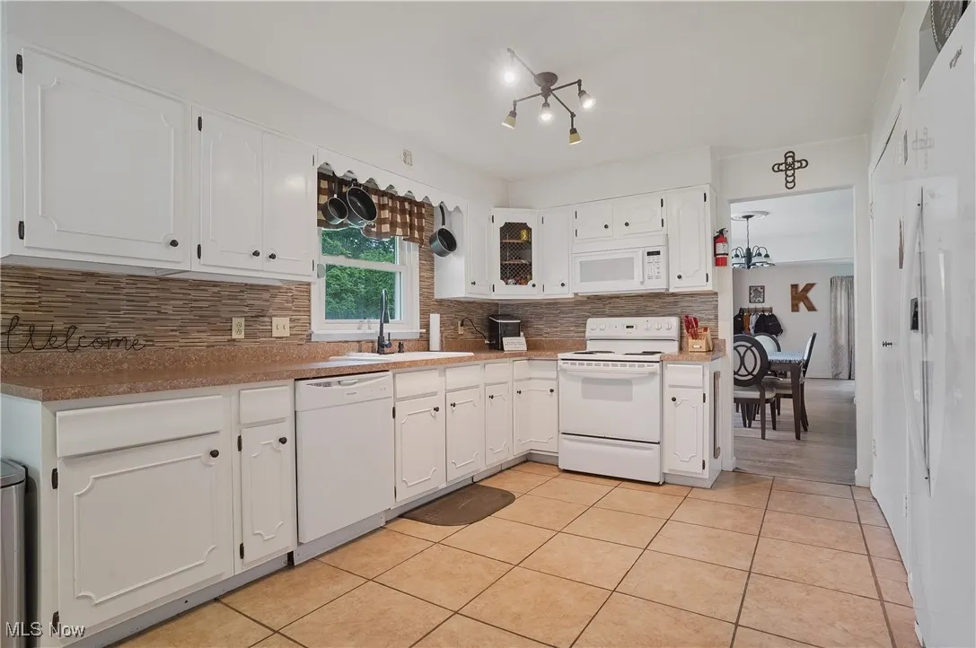 Kitchen with white cabinetry, white appliances, light tile patterned floors, and decorative backsplash