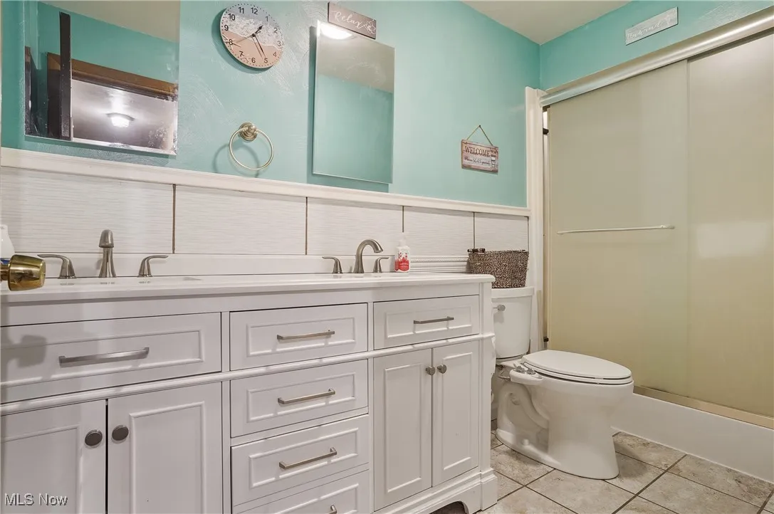Bathroom featuring light tile patterned floors, double vanity, and a shower stall