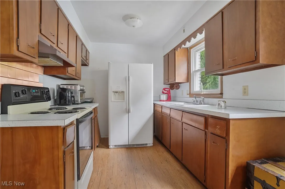Kitchen with white appliances, brown cabinetry, light wood-style floors, and under cabinet range hood