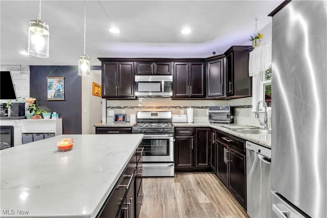 Kitchen featuring appliances with stainless steel finishes, pendant lighting, light wood-type flooring, dark brown cabinets, and decorative backsplash