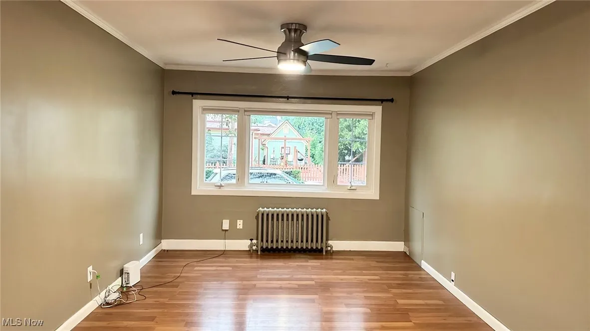 Living room featuring radiator, light wood floors, crown molding, and a ceiling fan
