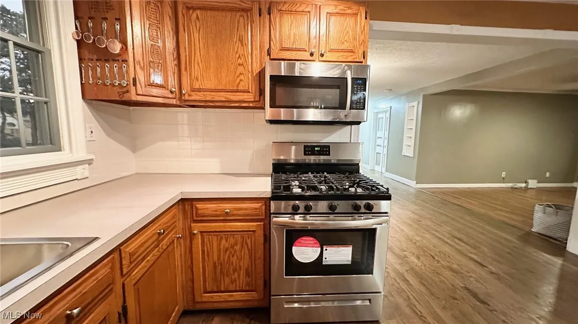 Kitchen featuring appliances with stainless steel finishes, brown cabinetry, backsplash, light countertops, and dark wood floors