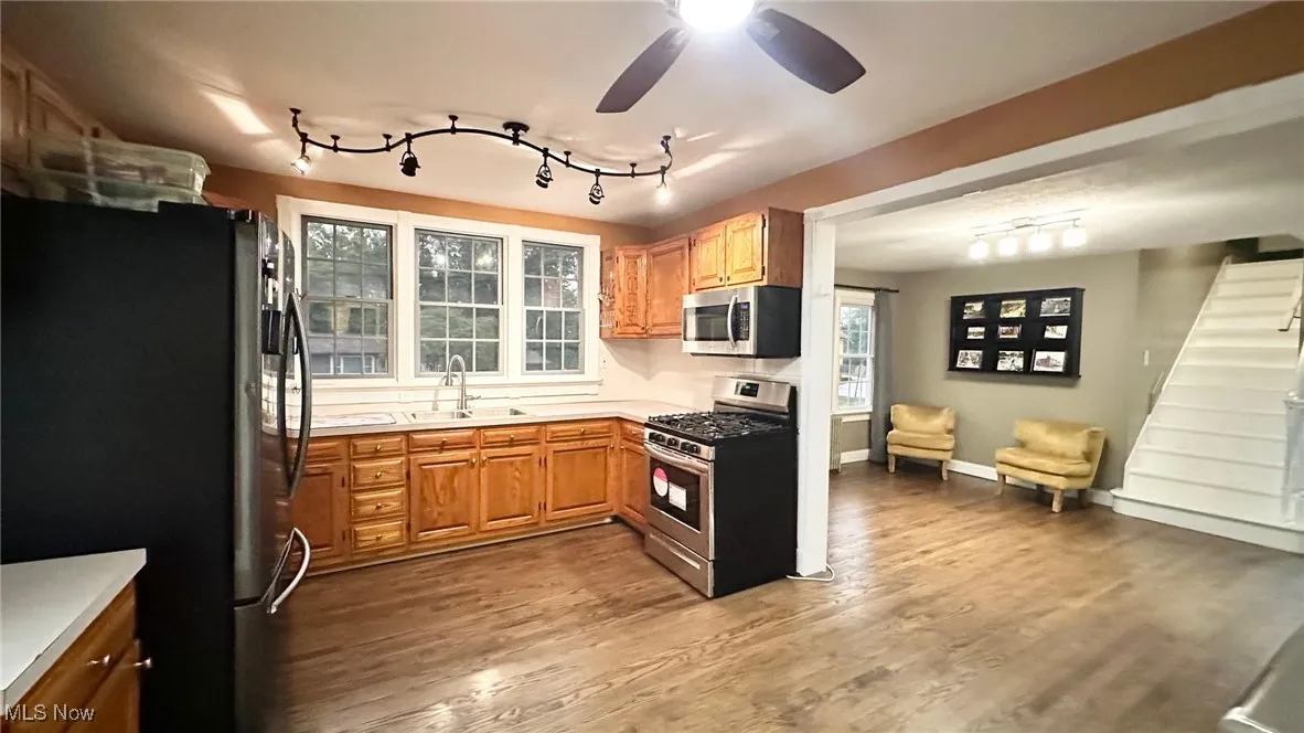 Kitchen featuring appliances with stainless steel finishes, light countertops, dark wood flooring, rail lighting, and brown cabinets