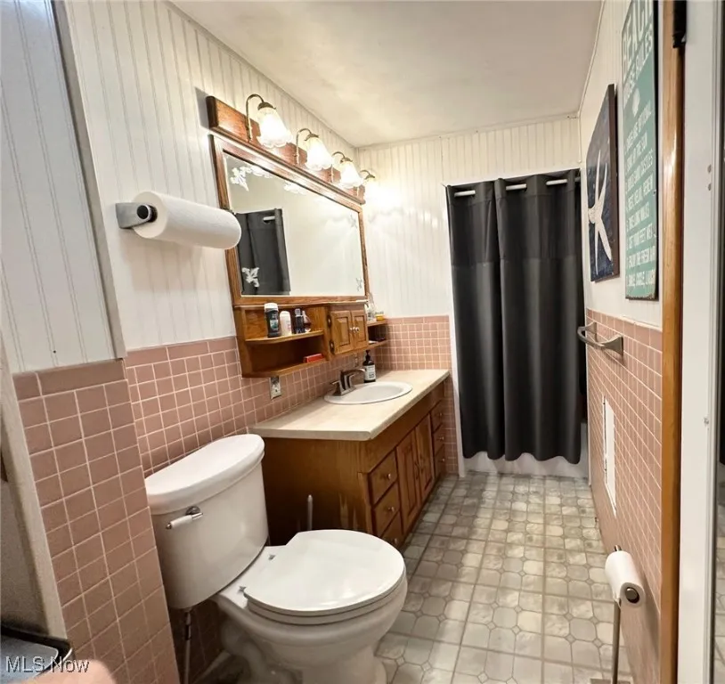 Bathroom featuring tile walls, a wainscoted wall, vanity, and light tile patterned flooring