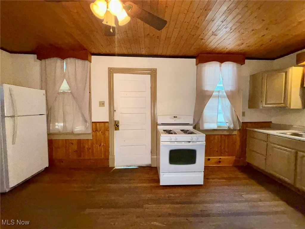 Kitchen with wood walls, a wainscoted wall, white appliances, dark wood finished floors, and wood ceiling
