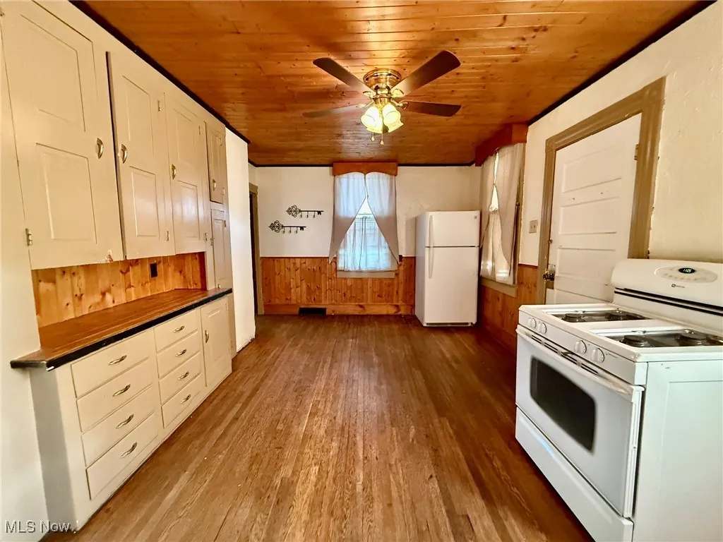 Kitchen with a wainscoted wall, wood walls, white appliances, light wood finished floors, and wood ceiling